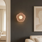 Pink petal-textured glass wall sconce with centered glowing bulb, compact floral shape