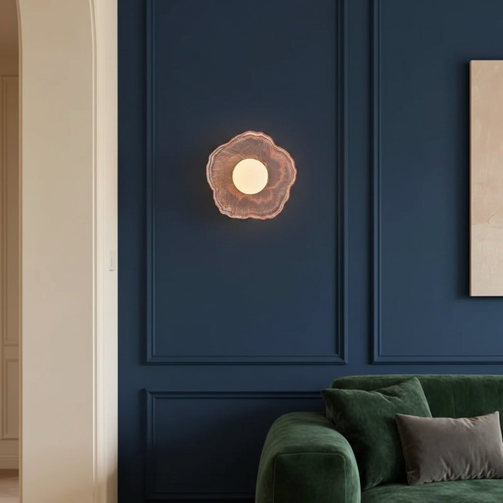 Coral pink flower-shaped wall sconce with round lit bulb and textured glass petals