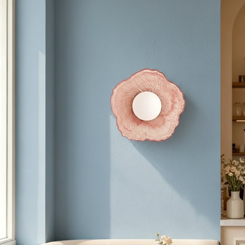 Pink petal glass wall light with a centered glowing bulb and scalloped flower rim