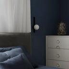 Wall globe sconce with small opal sphere and dark vertical arm beside bed
