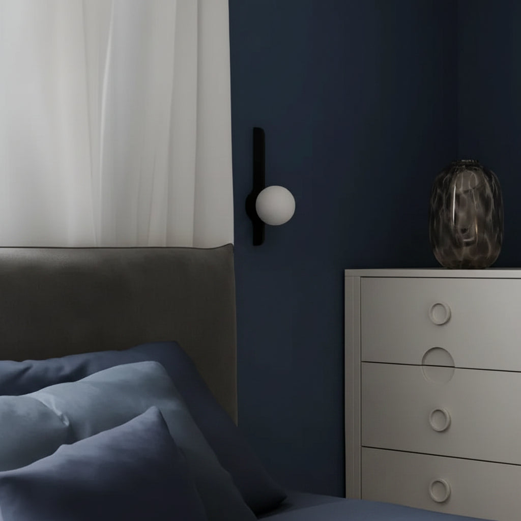 Wall globe sconce with small opal sphere and dark vertical arm beside bed