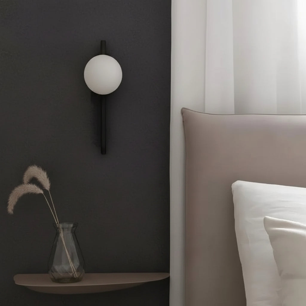 Wall globe sconce with white opal sphere and dark vertical arm in bedroom setting