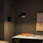Black hinged swing-arm dome wall light, angled head with glowing bulb