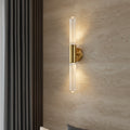 Minimalist wall light with clear fluted glass tube and brass backplate, lit warm.