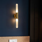Cylindrical wall sconce with clear fluted glass tube and brass arm, warm glow on.