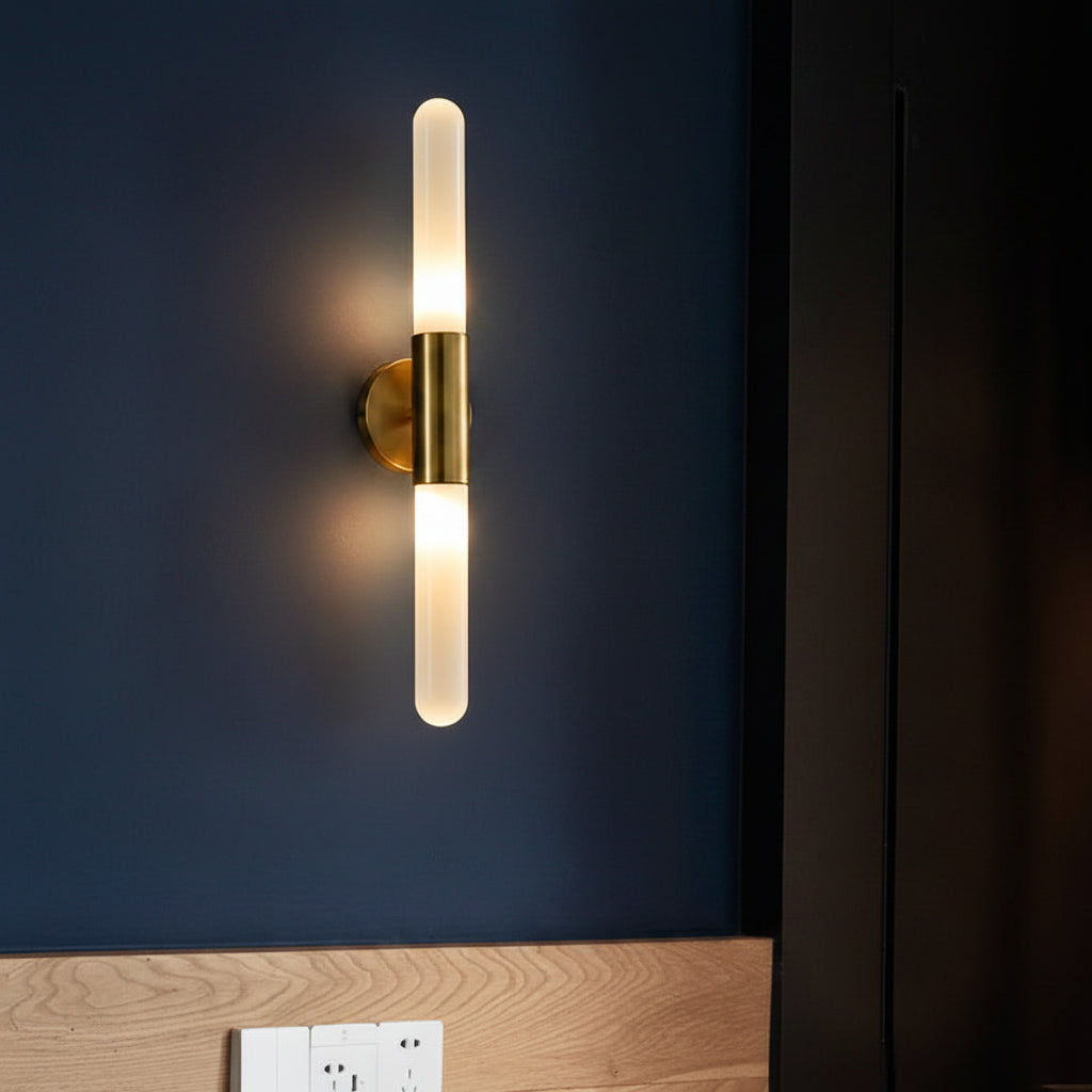 Cylindrical wall sconce with clear fluted glass tube and brass arm, warm glow on.