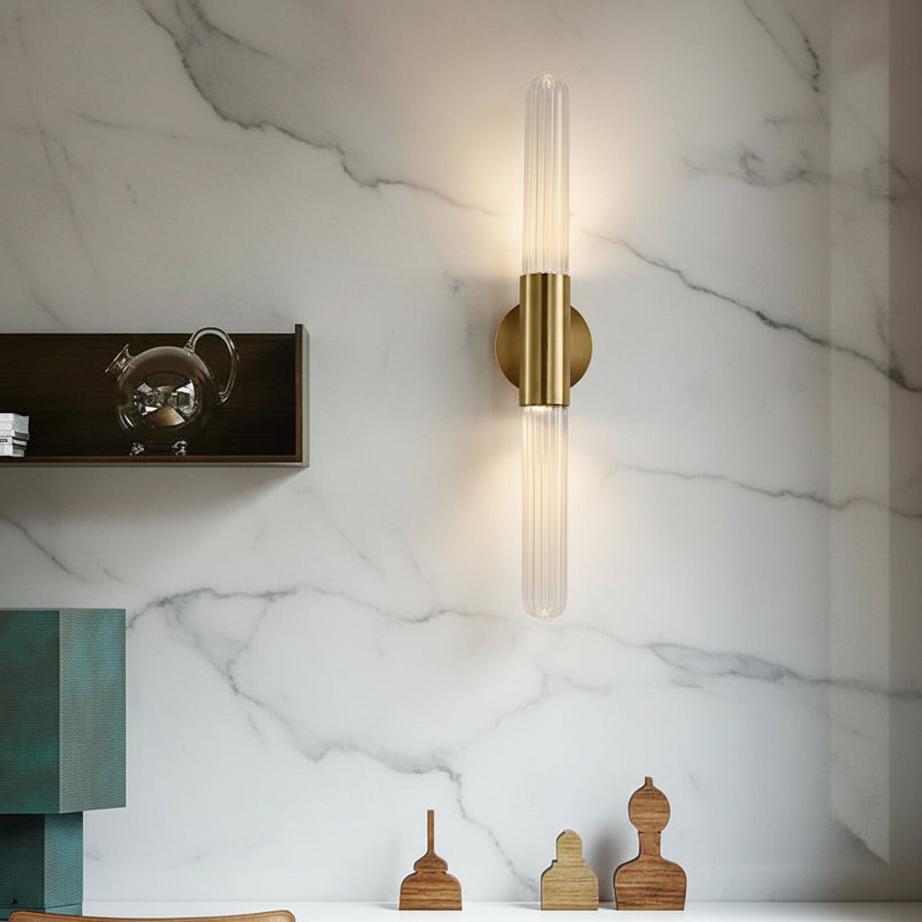 Tubular wall light with clear fluted glass cylinder and round brass mount, warm lit.