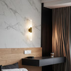 Modern wall sconce: clear fluted glass tube set in brushed brass wall bracket, lit.