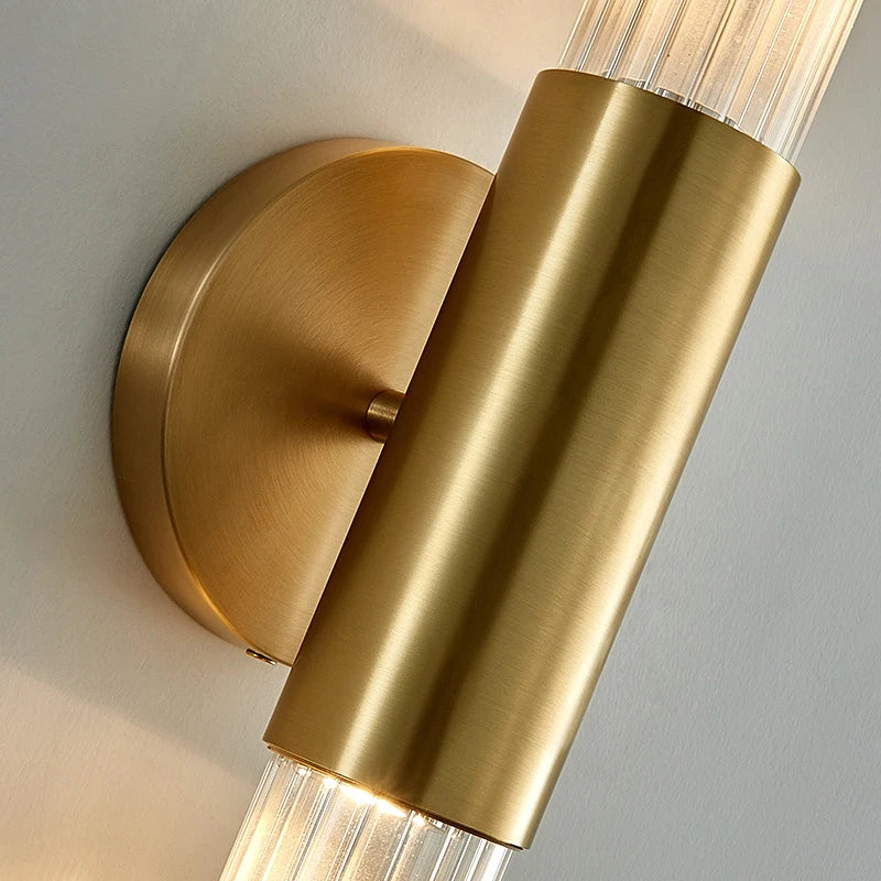 Close-up of brass wall mount and clear fluted glass tube on tubular wall sconce.