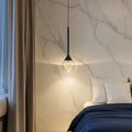 Teardrop pendant light with black cord and clear glass shade, warm moonlike inner glow