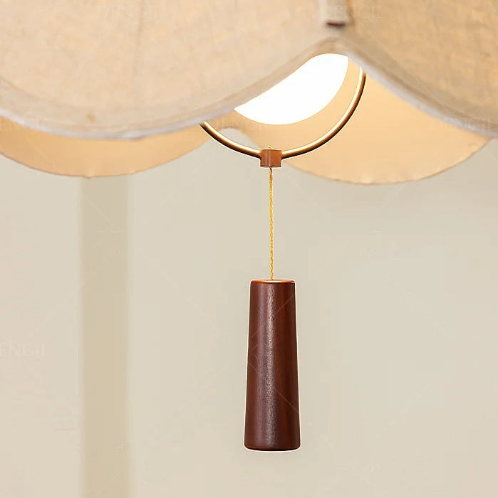 Brown pendant light finial with thin gold cord hanging from the fabric shade