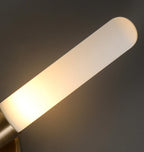 Detail view of long white diffuser tube on brass wall sconce, warm light glow.