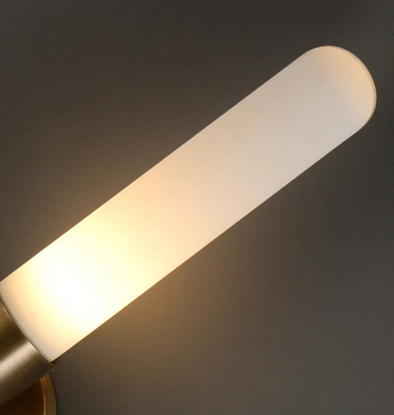 Detail view of long white diffuser tube on brass wall sconce, warm light glow.