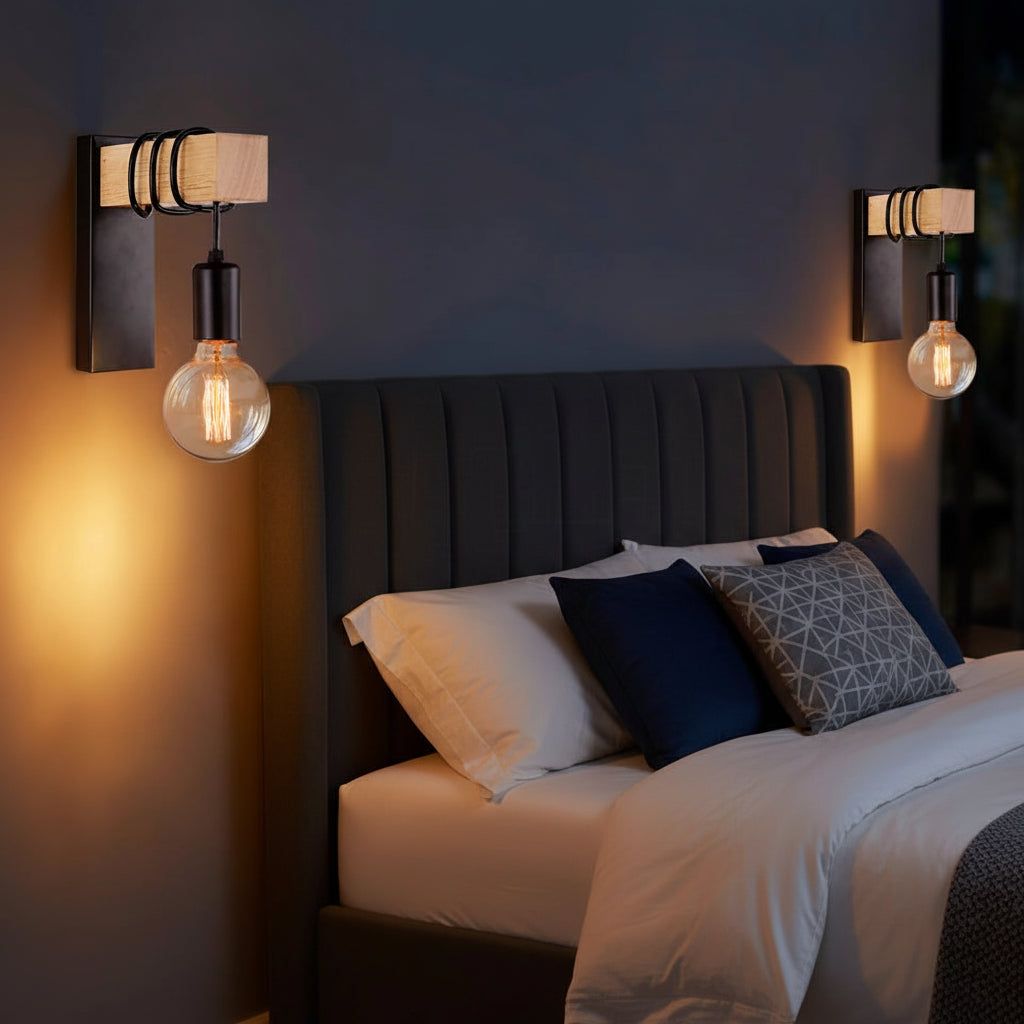 Pair of industrial wall sconces with black shades and glowing filament bulbs beside bed