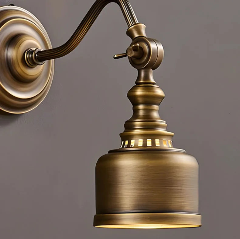 Close-up brass wall sconce details: curved arm, backplate, and cylindrical shade