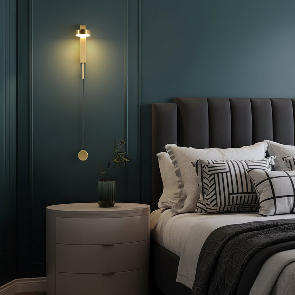 Gold vertical wall sconce with cylindrical lamp body and pull-switch knob, warm glow