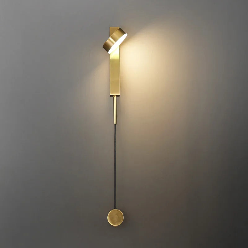 Gold vertical wall sconce with cylindrical lamp shade and round pull-switch knob