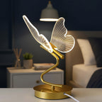 Gold butterfly table lamp with glowing wire wings on a round base and curved stem