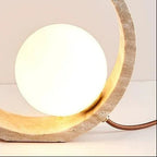 Round globe table lamp with glowing bulb inside textured ring and brown cord