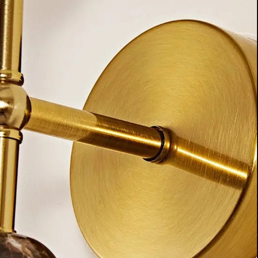 Brass arm and circular backplate detail of stacked wall sconce with frosted shade