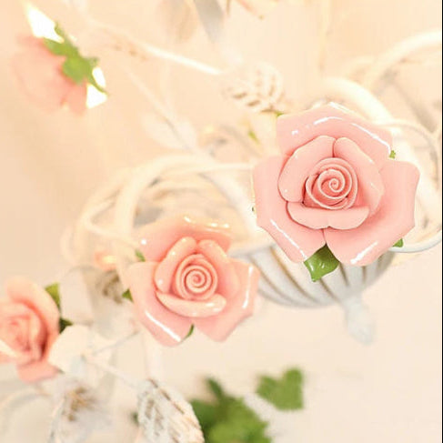 Pink fabric rose details on a white chandelier arm with curling scroll wire