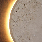 Close-up of glowing edge around speckled travertine panel in a round wall sconce