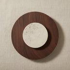 Brown circular sconce with textured travertine center disk and warm backlight