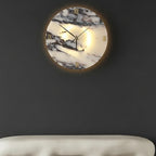 Round backlit marble wall clock light with Roman numerals and black hands on dark wall