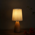 Warm-lit conical table lamp with pleated beige shade and dark wood-grain ceramic base