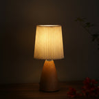 Warm-lit conical table lamp with pleated beige shade and dark wood-grain ceramic base