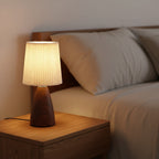 Conical table lamp with pleated beige shade and dark wood ceramic base on side table