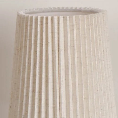 Pleated beige fabric lampshade with scalloped rim on a conical table lamp