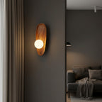 Oval wood backplate wall sconce with glowing bulb mounted on wall