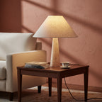 Conical fabric table lamp with speckled travertine pedestal base on a bedside table