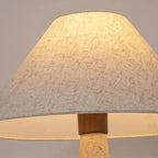Conical fabric lamp shade atop a speckled travertine pedestal base