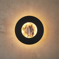 Round black wall light with marble backlit center in warm yellow glow