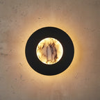 Round black wall light with marble backlit center in warm yellow glow