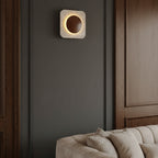 Square travertine wall sconce with backlit circular cutout and warm halo