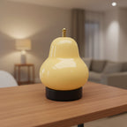 Cream gourd-shaped lamp glowing with gold top and black base on table.